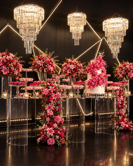 Mesa de doces sobre cubos de acrílico iluminados em rosa, sob lustres de cristal
