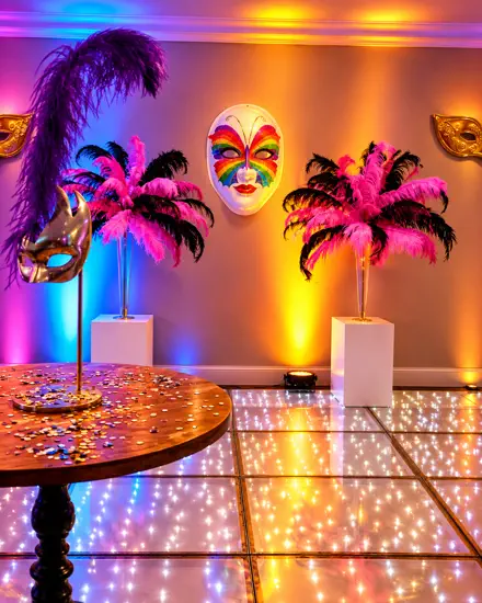 Máscaras e plumas em pedestais, uplight colorido na parede e pista de LED estrelada